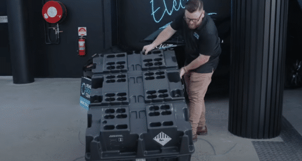 A man is maneuvering a large black crate on a trolley in a garage-like setting.